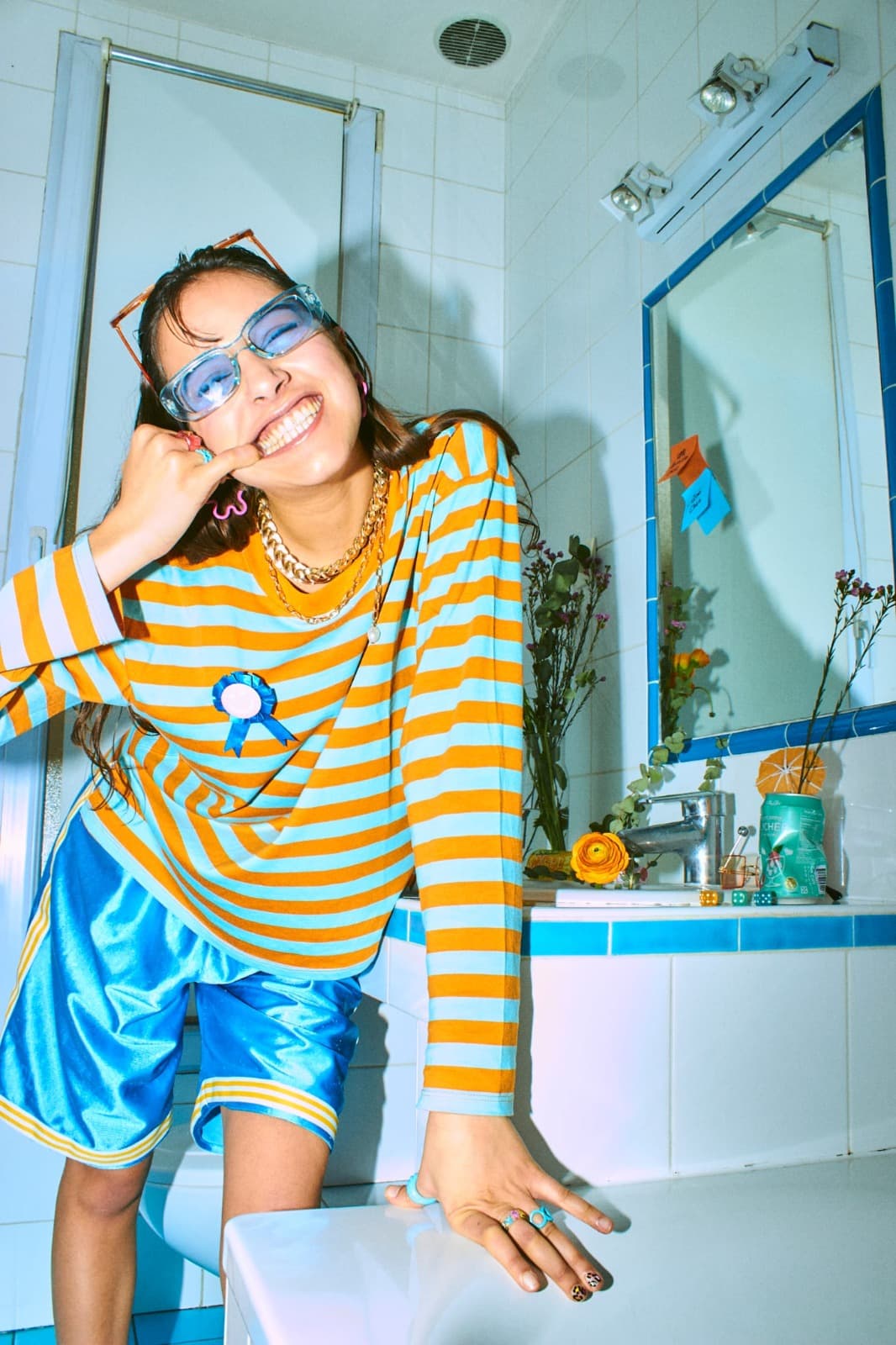 Qiwi Chee riant largement, une rosette bleue épinglée sur son pull rayé, appuyée sur le rebord d’un lavabo.
